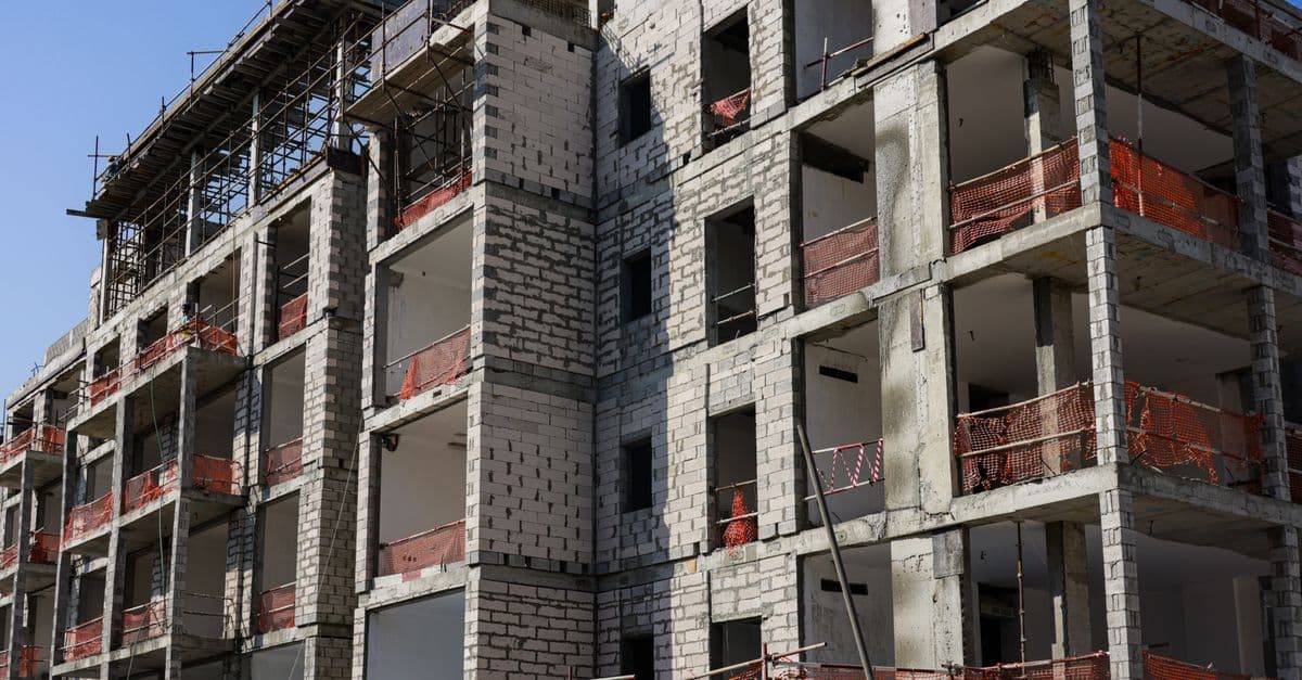 A modern multi-story apartment building under construction with scaffolding and safety netting.