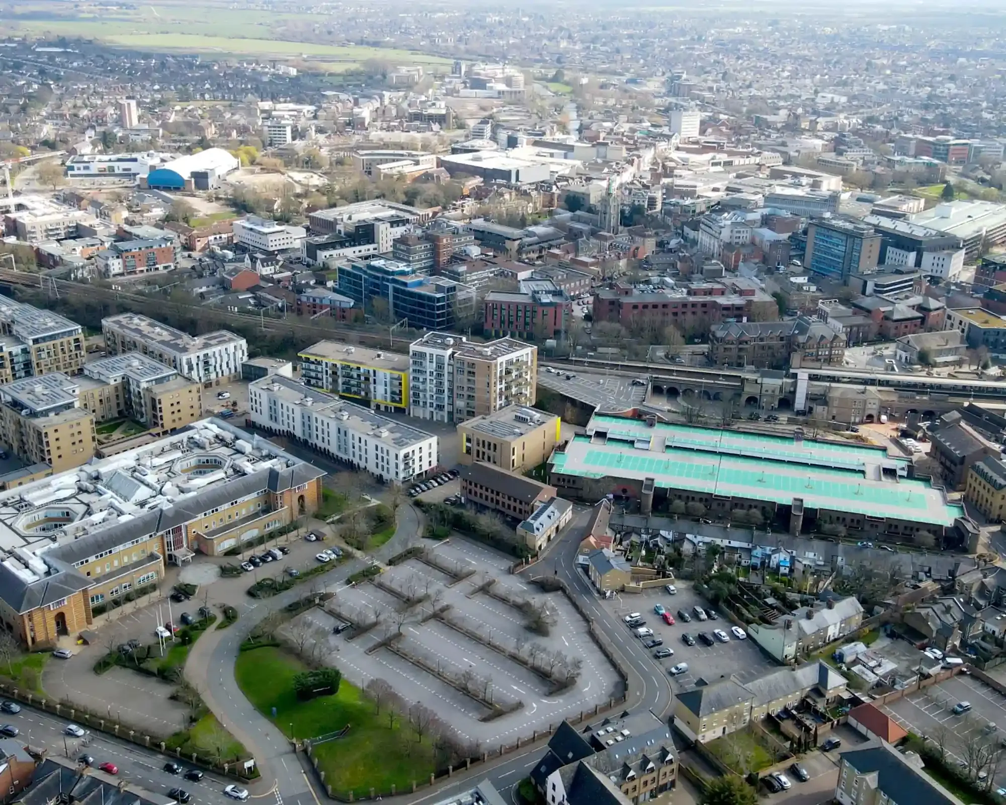 Aerial view of Chelmsford city centre with modern apartment blocks, the railway station and the cathedral spire among the rooftops.