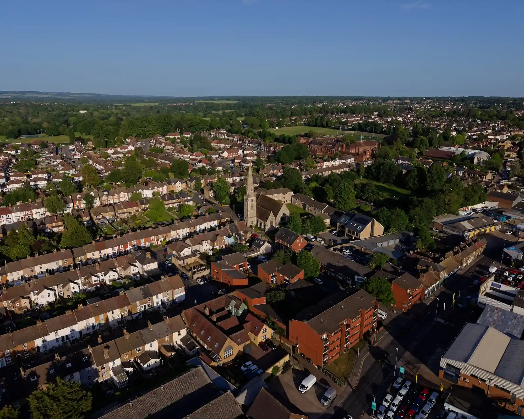 Aerial view over rows of Victorian terraced houses and a church spire in Maidstone, with the North Downs on the horizon.