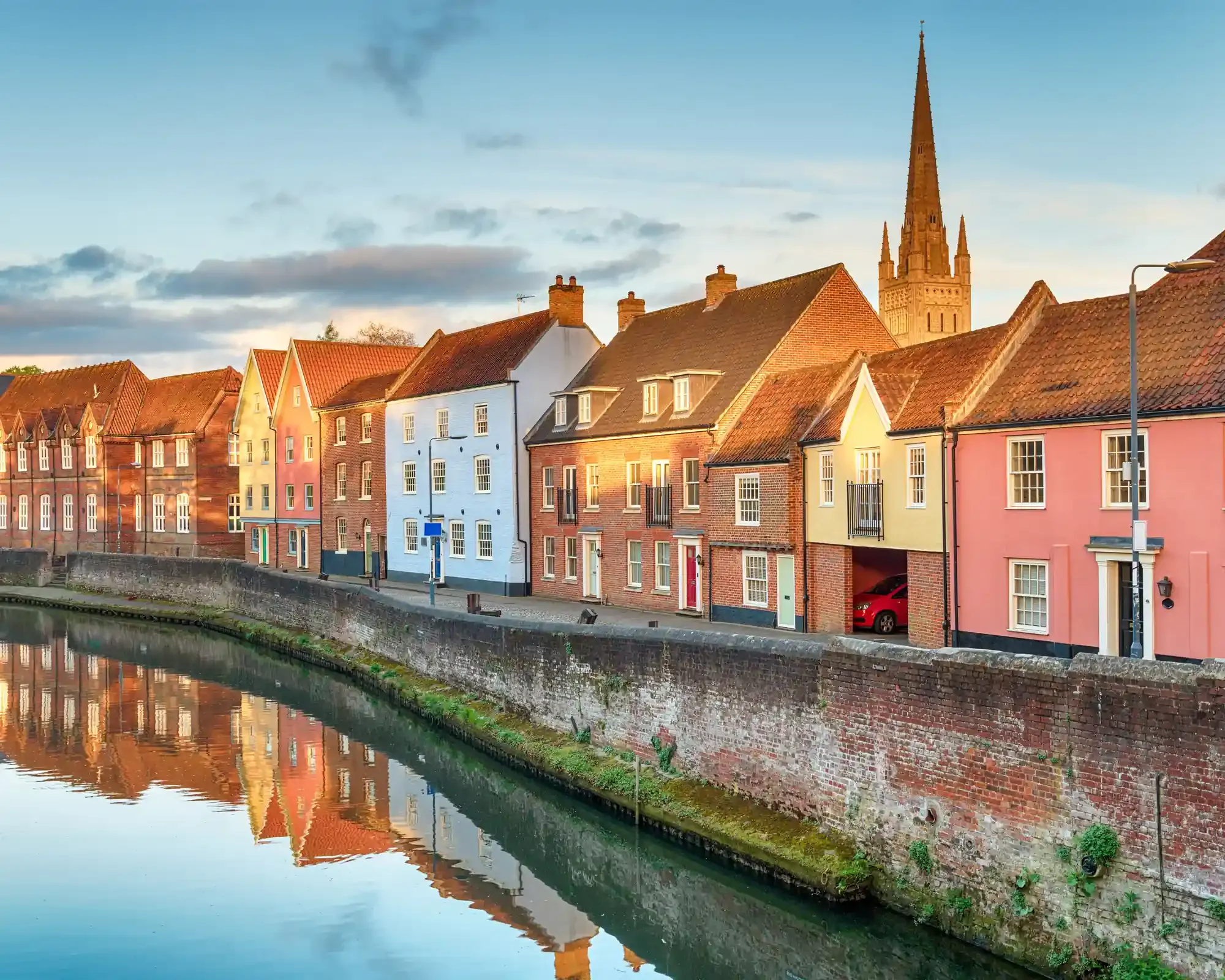 Colourful period houses along Quayside beside the River Wensum in Norwich, with the cathedral spire rising behind them.
