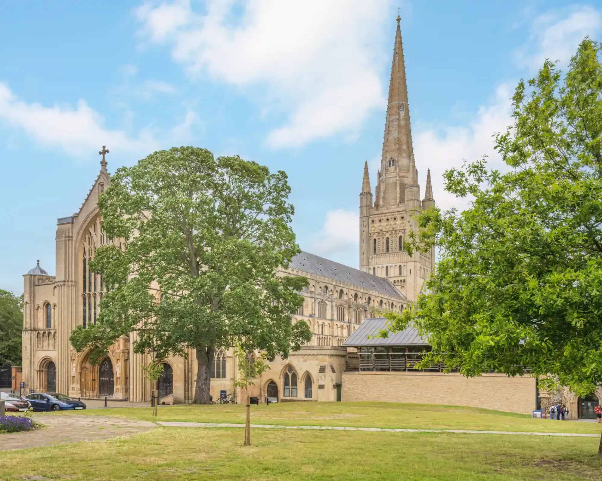 Norwich Cathedral's Norman west front and tall spire seen across the green of the Cathedral Close.