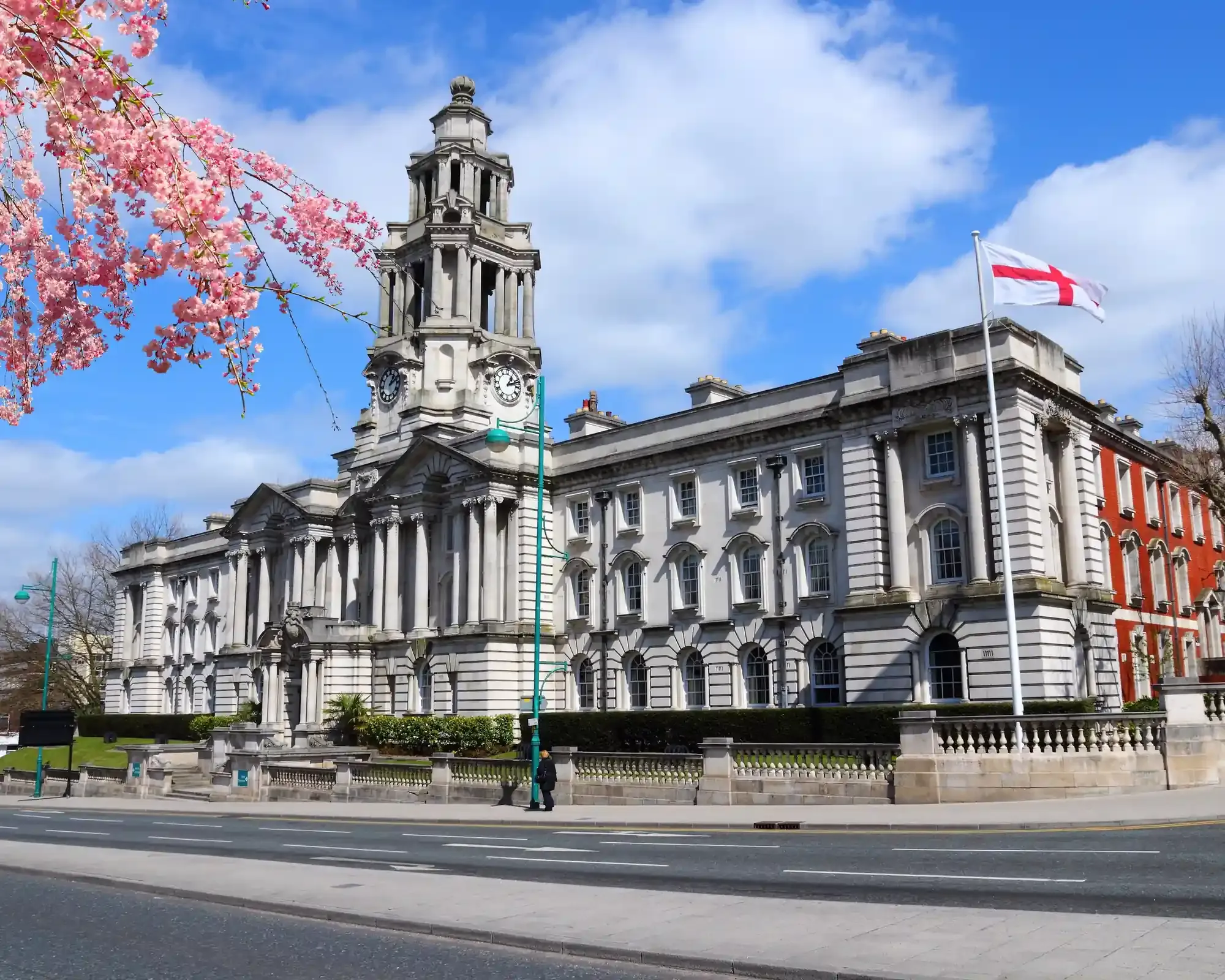Stockport Town Hall's white Portland stone clock tower and columned front, with pink cherry blossom in the foreground.