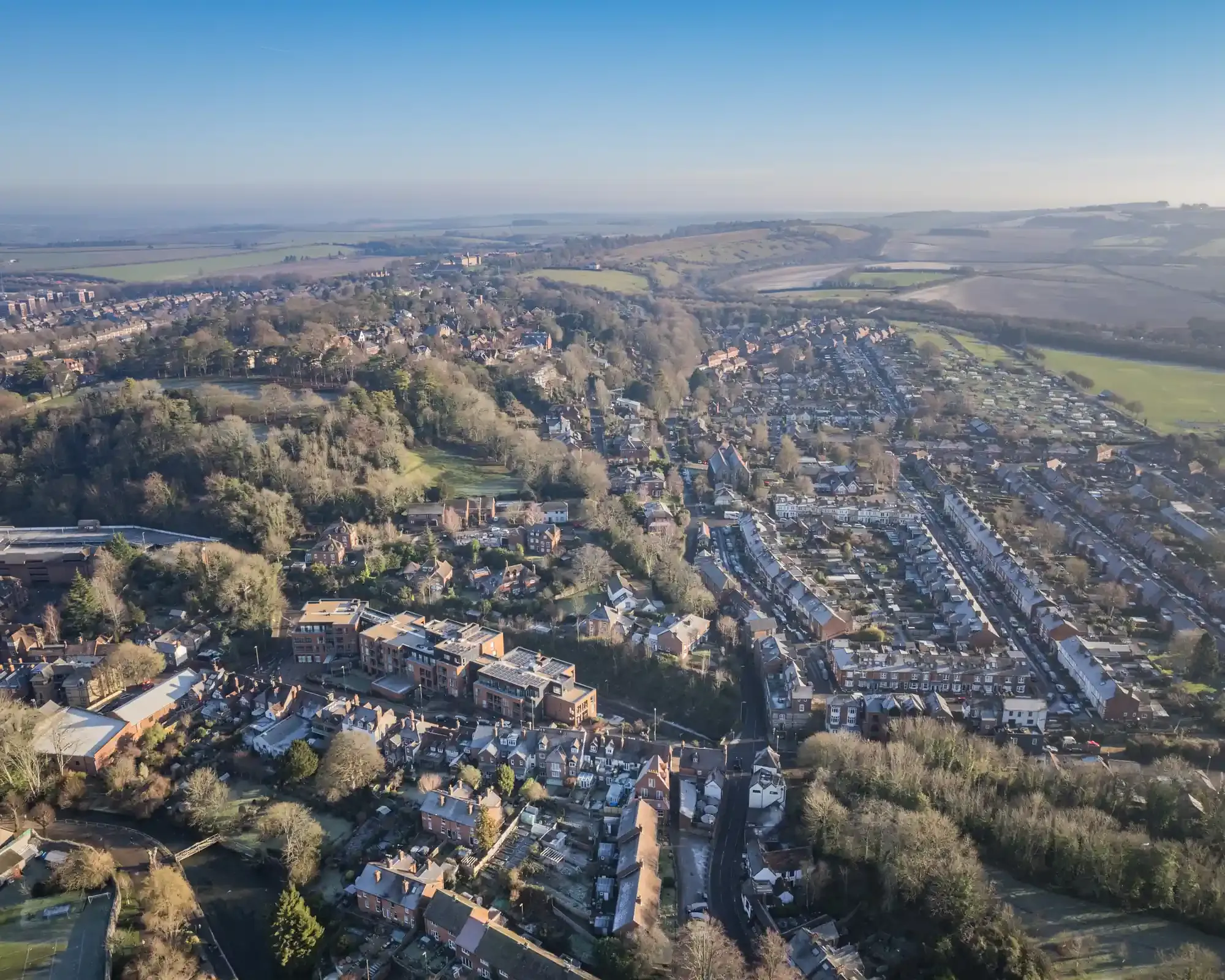 Aerial view over Winchester's Victorian terraced streets and wooded hillside, with the chalk downland of Hampshire beyond.