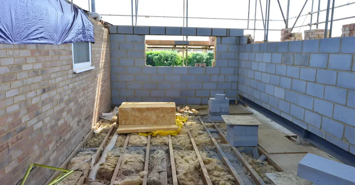 Single-storey rear extension under construction, with blockwork walls, floor joists, insulation and scaffolding