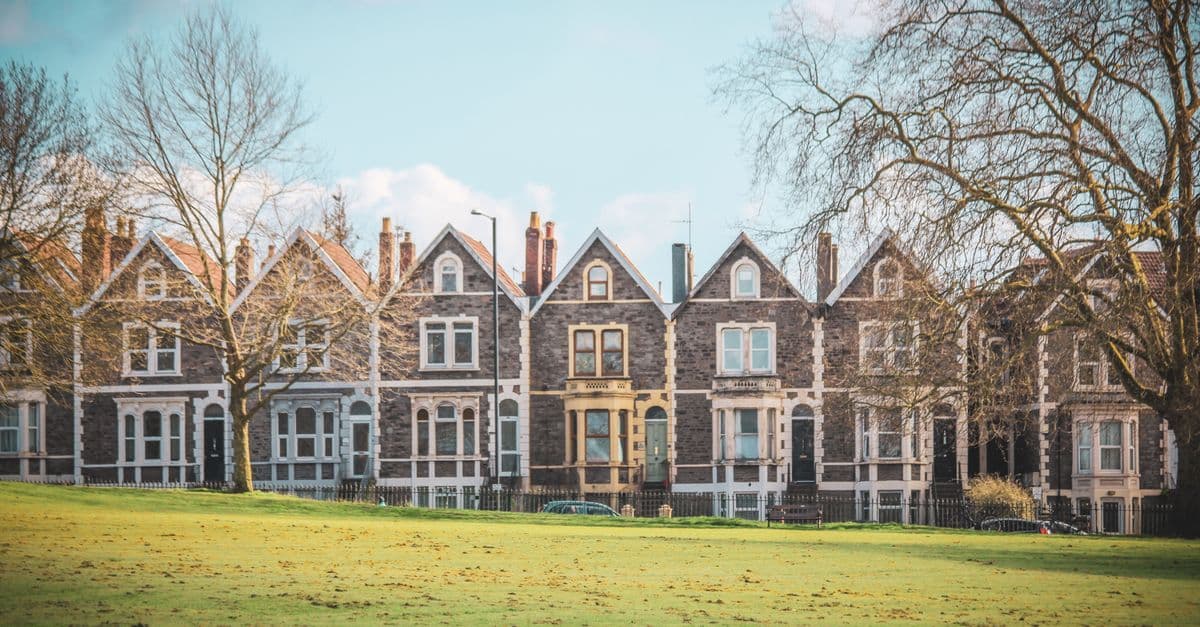 Victorian terraced houses in Bristol, England, set against a lush green park with clear skies.