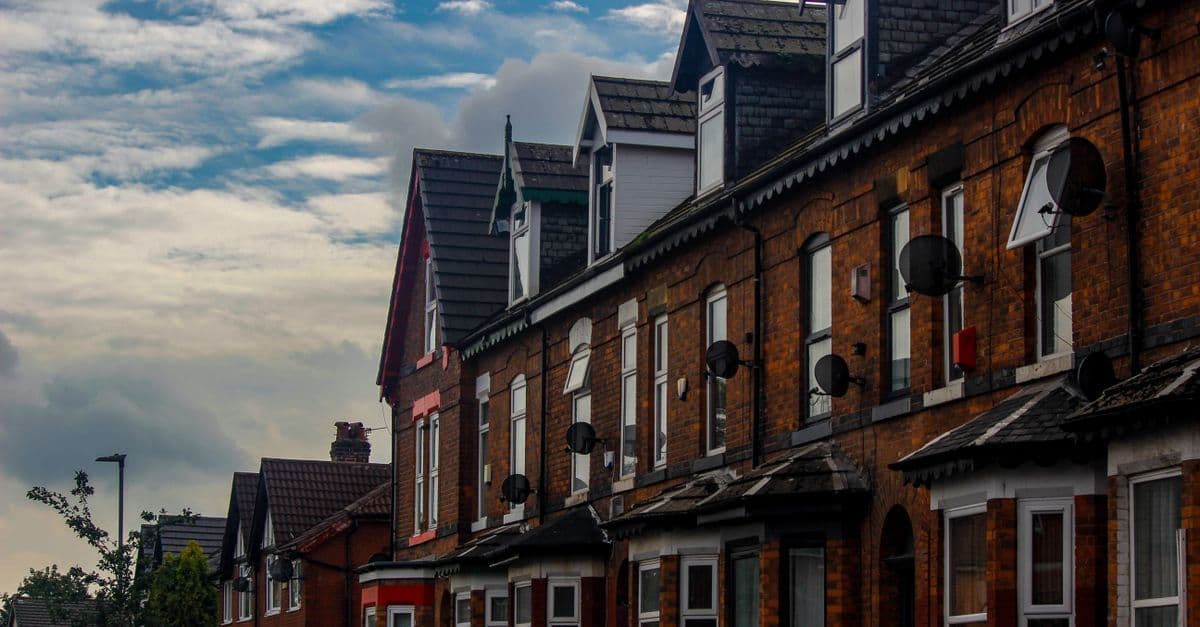 Traditional brick row houses in Manchester's suburb under a cloudy sky.