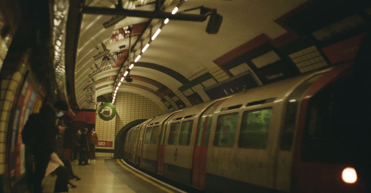 A subway train arrives at an underground station in London, UK, with commuters waiting on the platform.