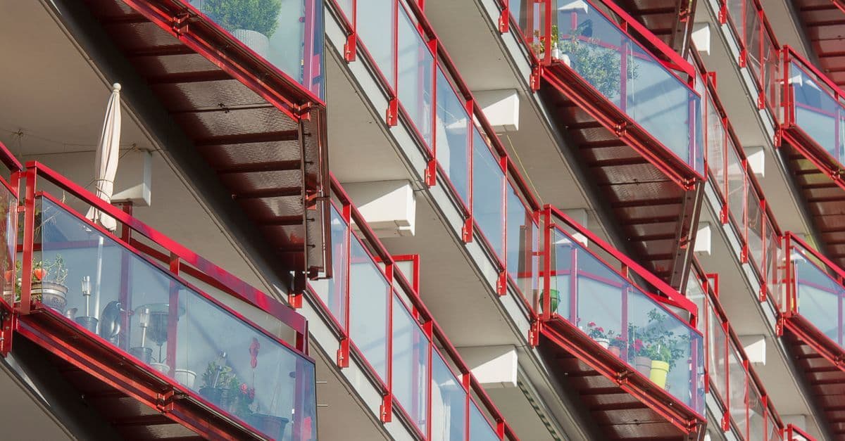 Dynamic view of modern urban apartment balconies featuring red railings and glass panels, showcasing contemporary architecture.