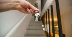 A hand holding house keys in a modern interior, symbolizing new home ownership or real estate investment.