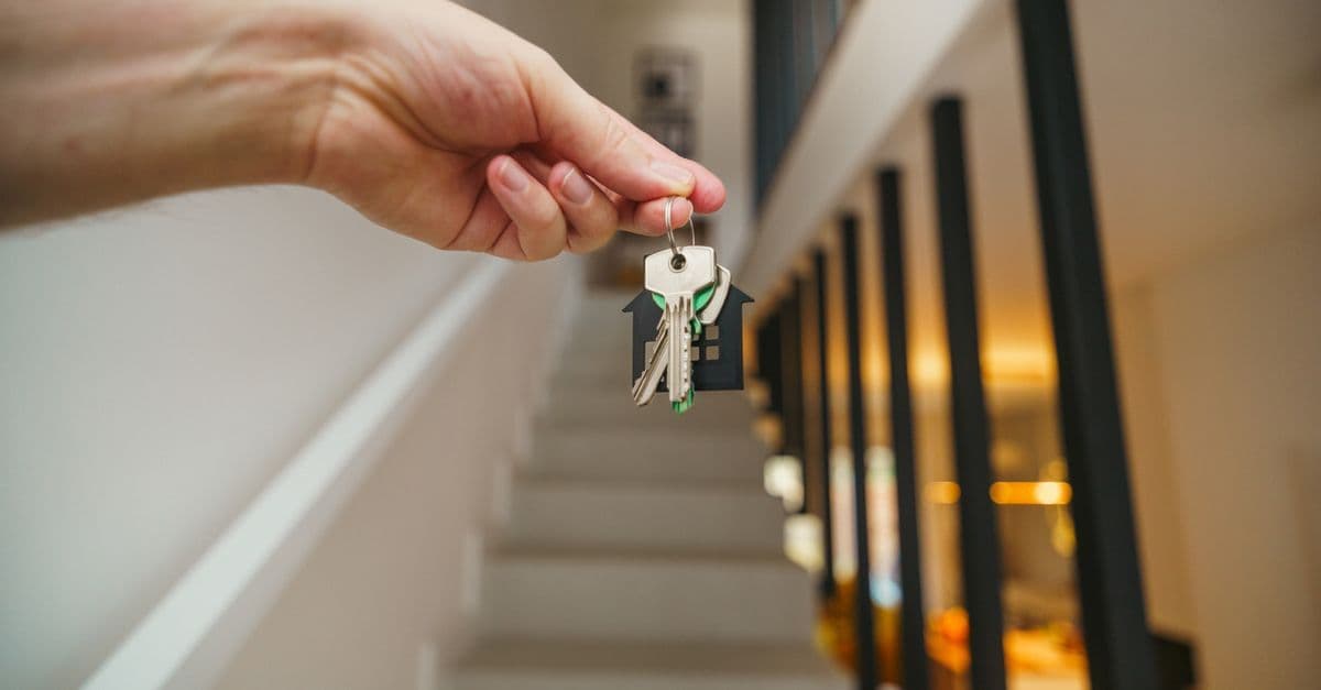 A hand holding house keys in a modern interior, symbolizing new home ownership or real estate investment.