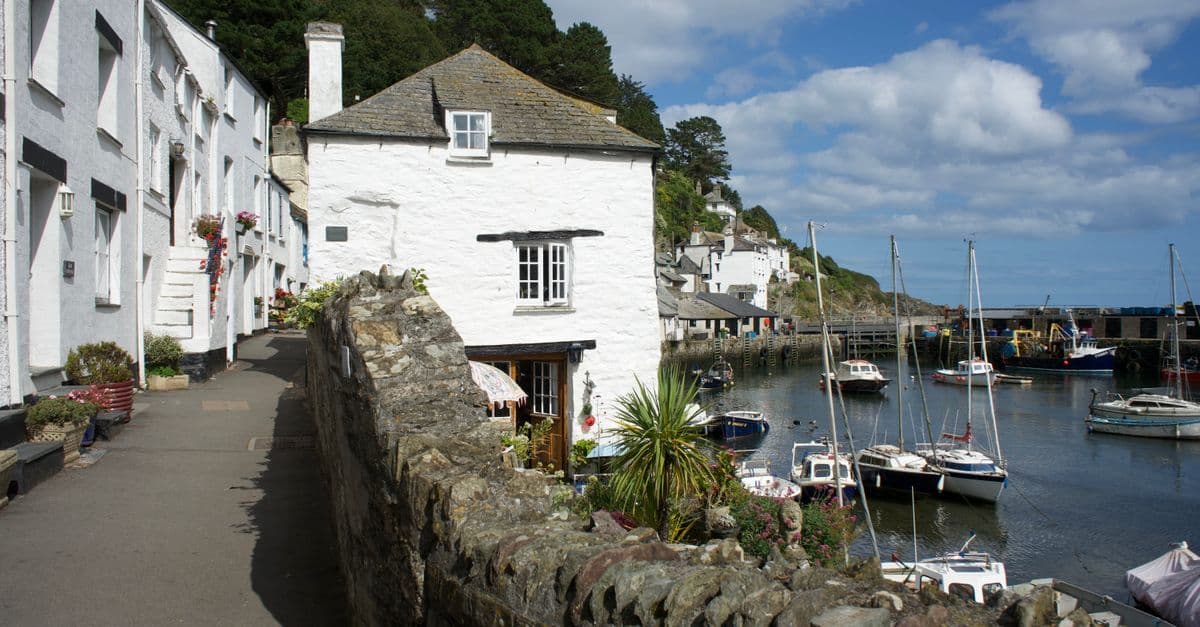 Picturesque scene of Polperro harbour with boats and historic cottages under a bright sky.