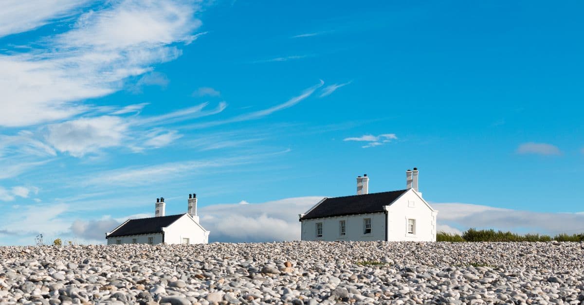 White cottages on a pebble beach under a clear blue sky in Wales.