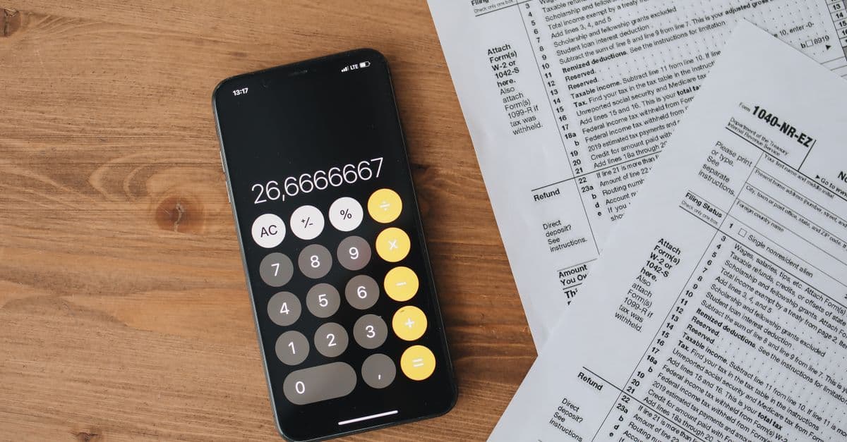 Overhead view of smartphone calculator and tax forms on a wooden table.