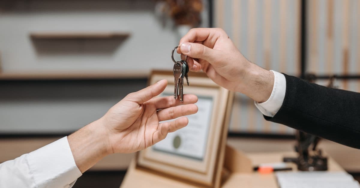 Detailed view of hands exchanging keys in a professional office environment, symbolizing real estate or business transactions.