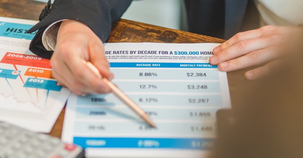 A close-up of hands analyzing mortgage rate documents with a pen and calculator in a business setting.