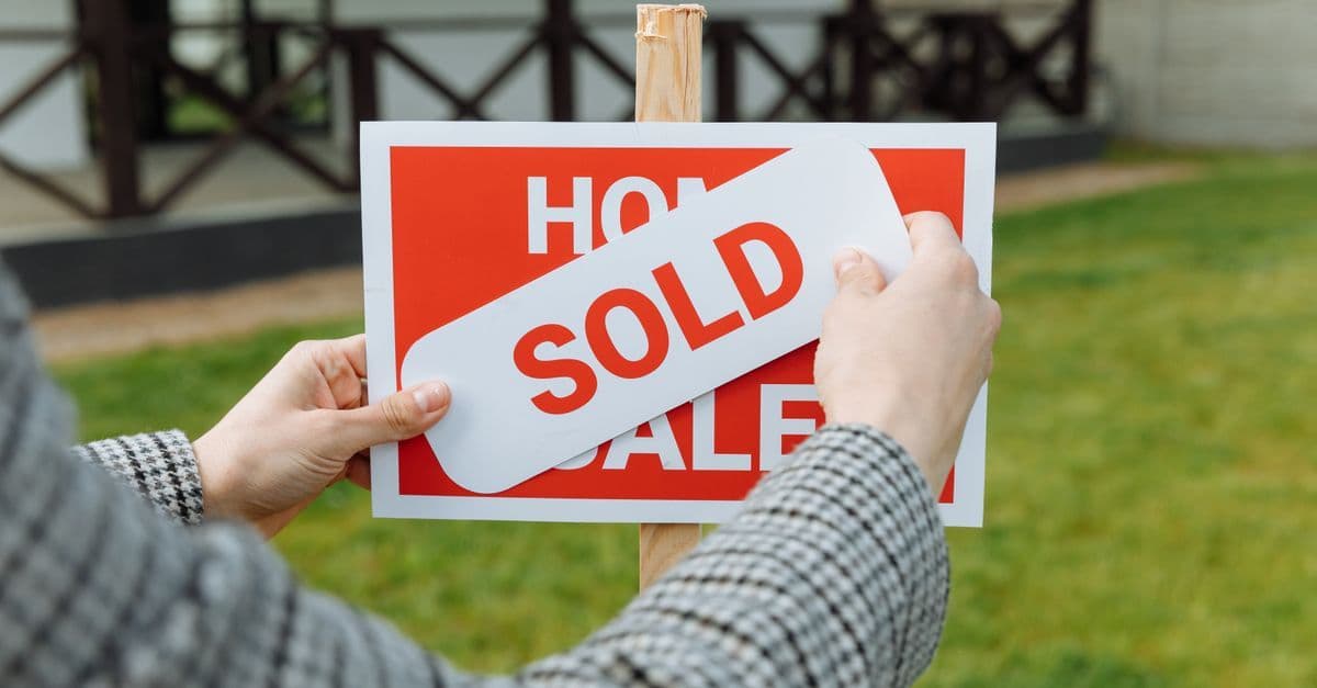 Close-up of hands placing a sold sticker on a real estate sign outside a house.