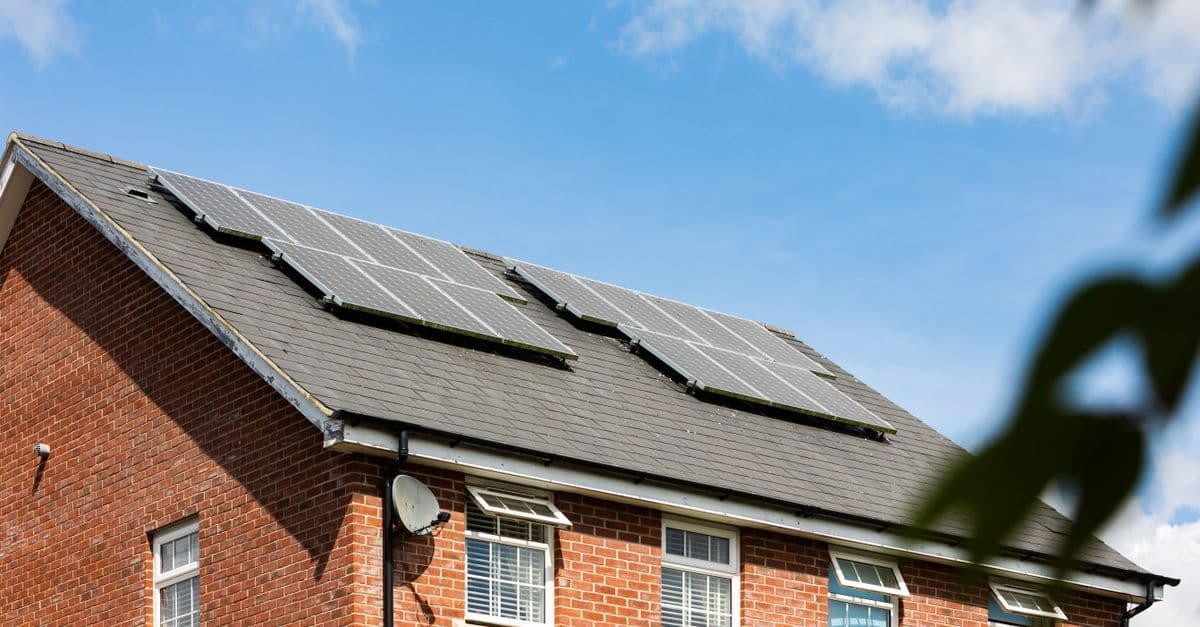 Brick house featuring solar panels on the roof under a clear blue sky, promoting sustainable energy.