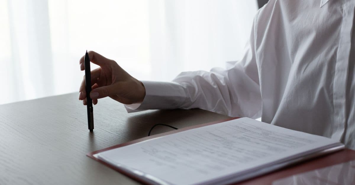 A woman examines documents, holding a pen over a table in a bright indoor setting.