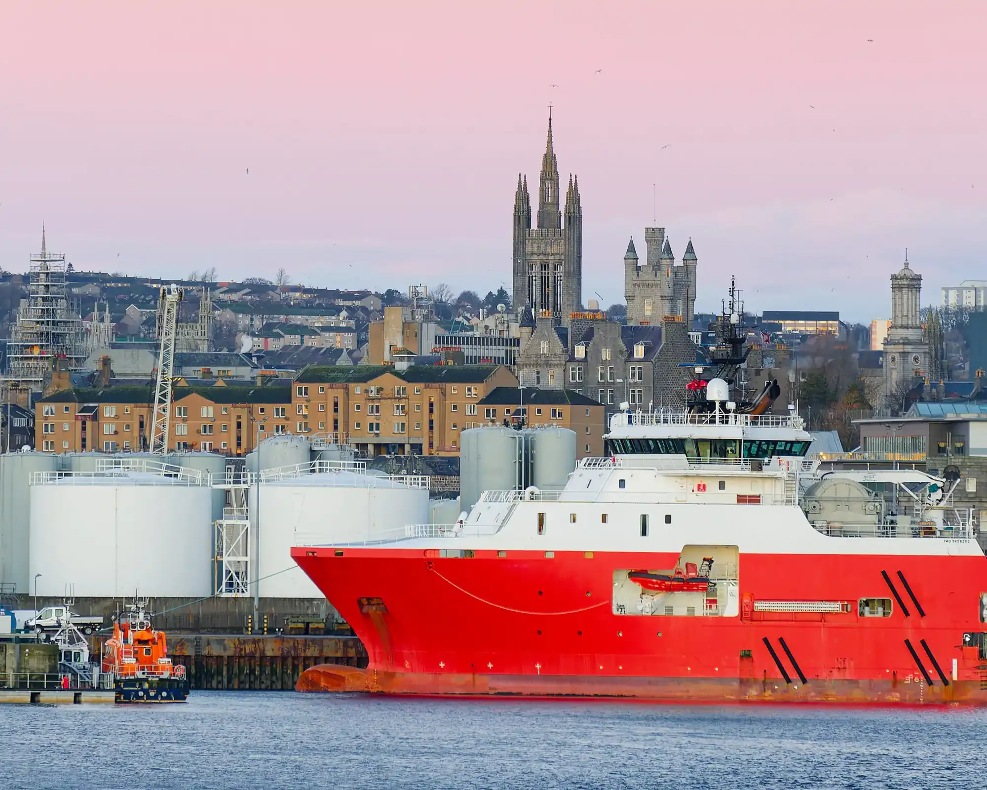 Aberdeen Harbour at dusk, with a supply ship in front of the city skyline and Marischal College’s spires.