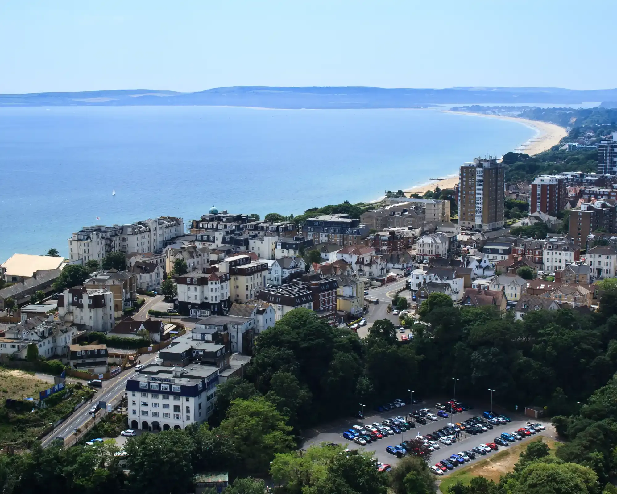 Aerial view of Bournemouth’s clifftop hotels and apartment blocks above the sandy beach, with Poole Bay and the Purbeck Hills beyond.