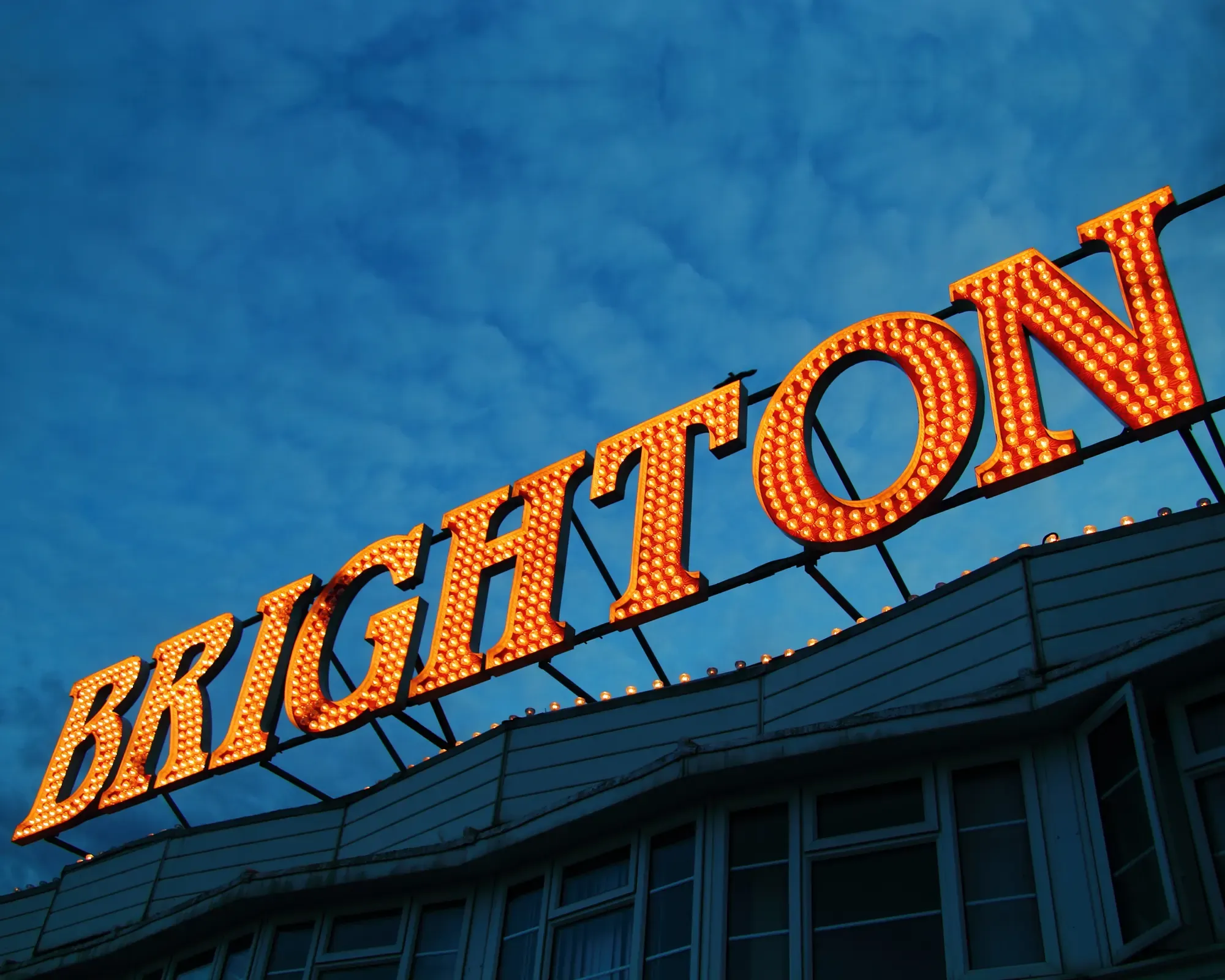 The illuminated "BRIGHTON" sign on Brighton Palace Pier, glowing orange against a deep blue evening sky.