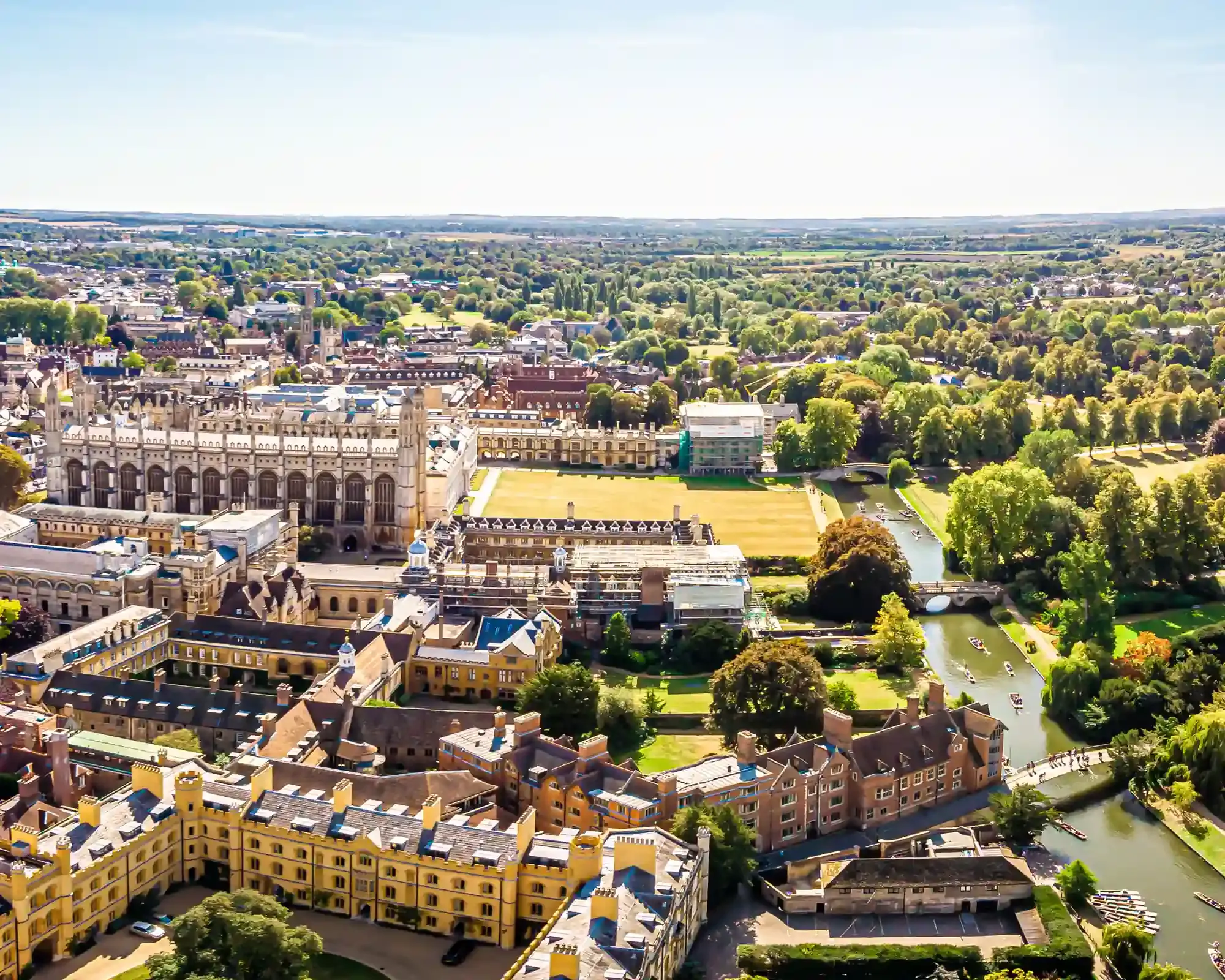 Aerial view of Cambridge on a sunny day, with King's College Chapel and college buildings beside the River Cam, where punts are out on the water.