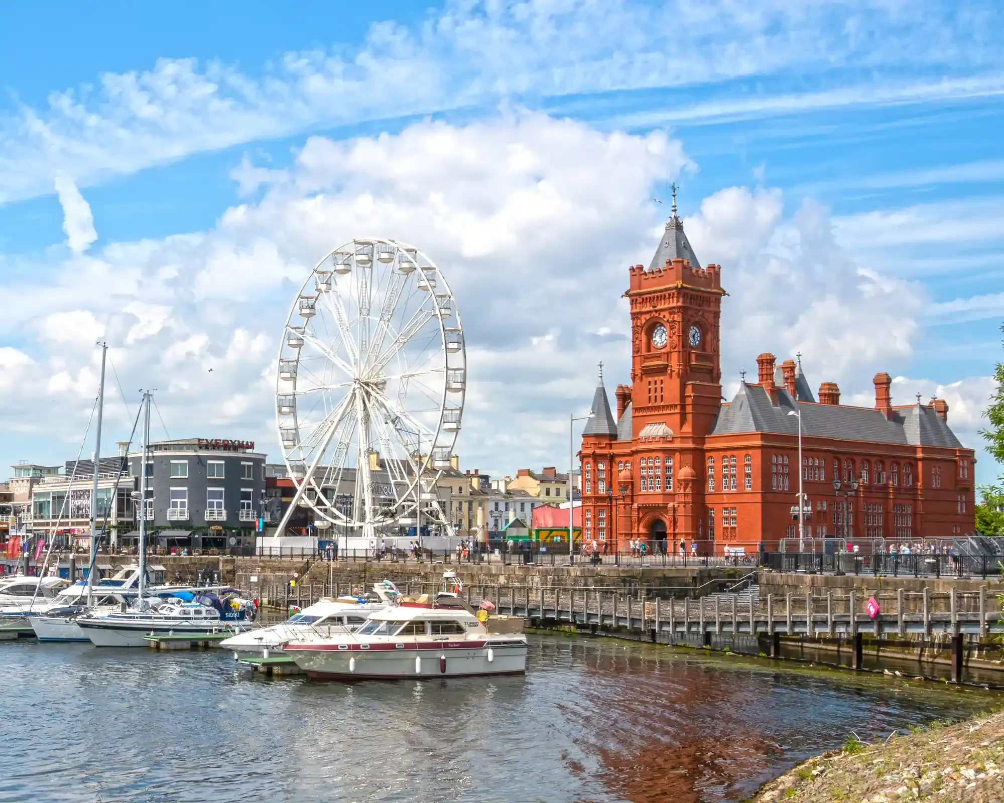Cardiff Bay on a sunny day, with the red-brick Pierhead Building, a big wheel and boats moored in the marina.