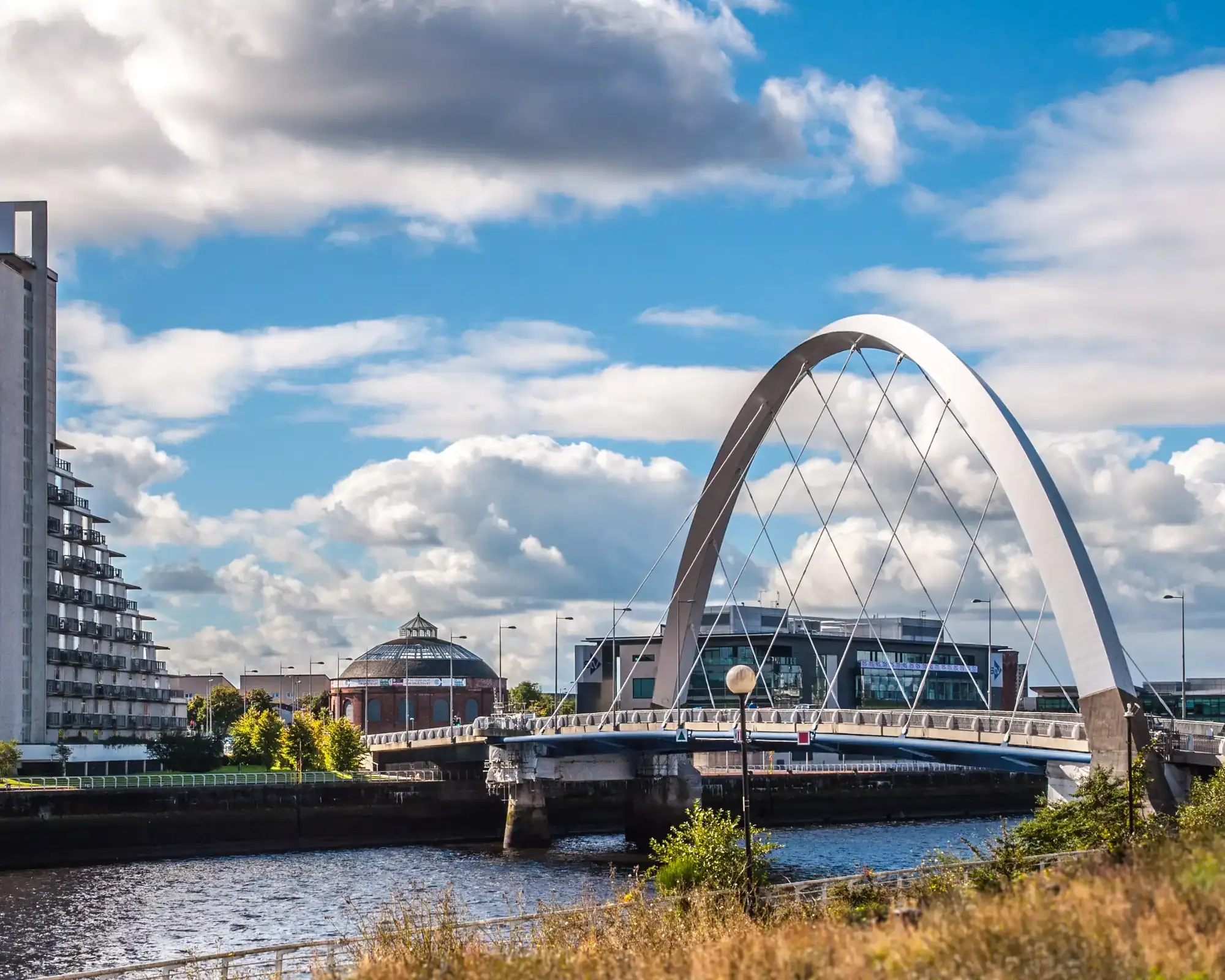 The Clyde Arc bridge over the River Clyde in Glasgow, with a riverside apartment tower and the rotunda in the background.