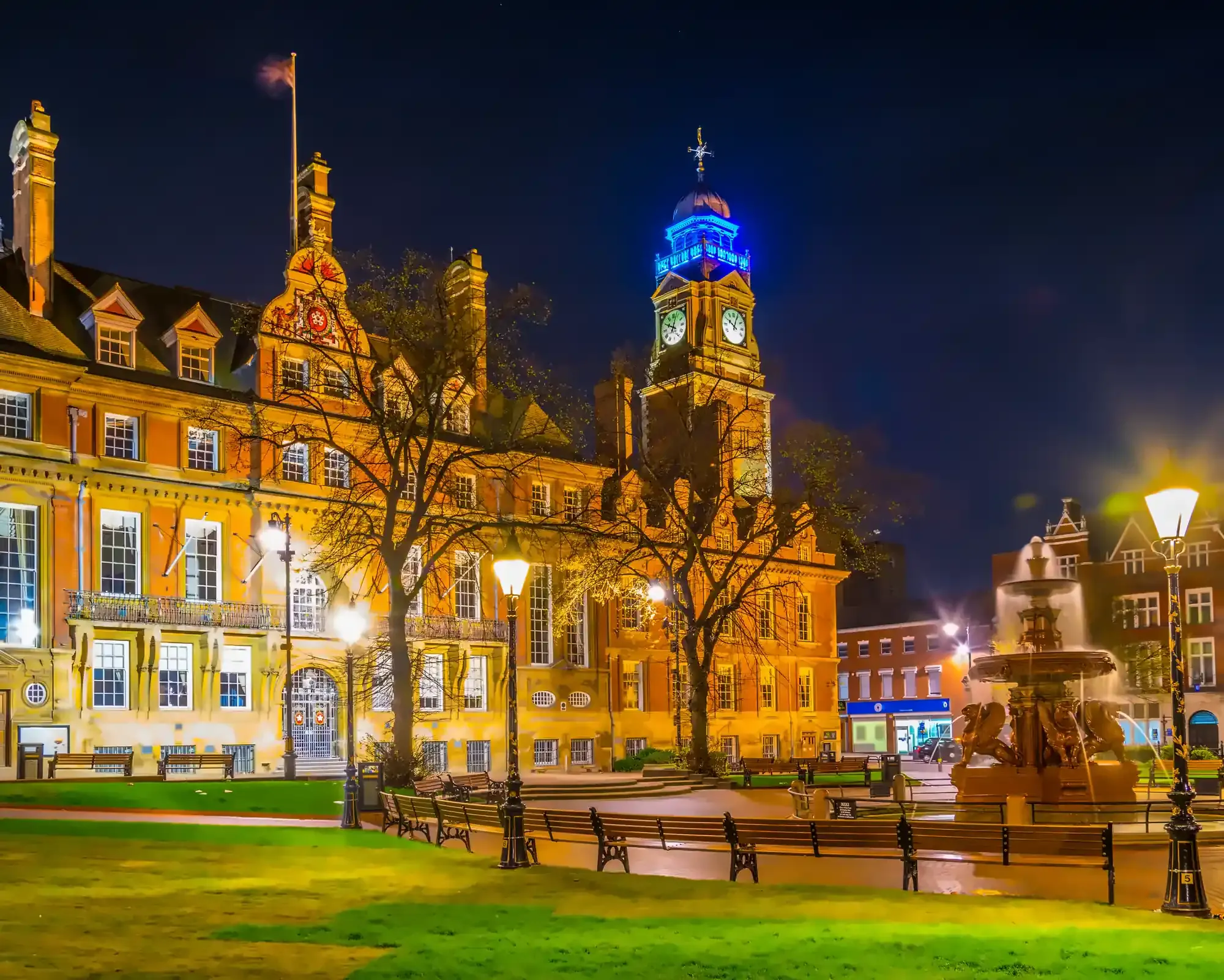 Leicester Town Hall at night, with its clock tower lit up in blue and the ornate fountain glowing in Town Hall Square.