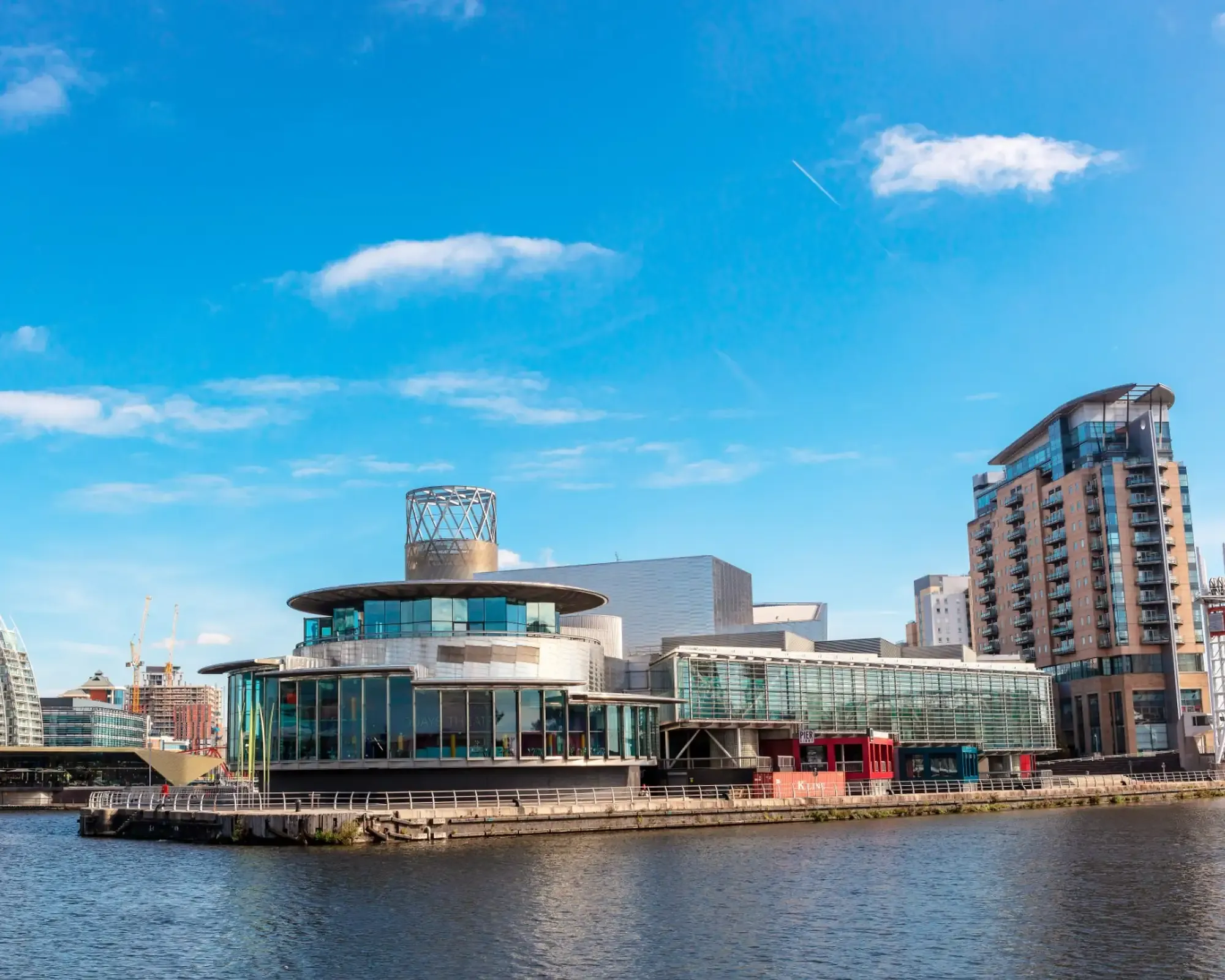 The Lowry arts centre at Salford Quays on a sunny day, with modern apartment blocks beside the water under a blue sky.