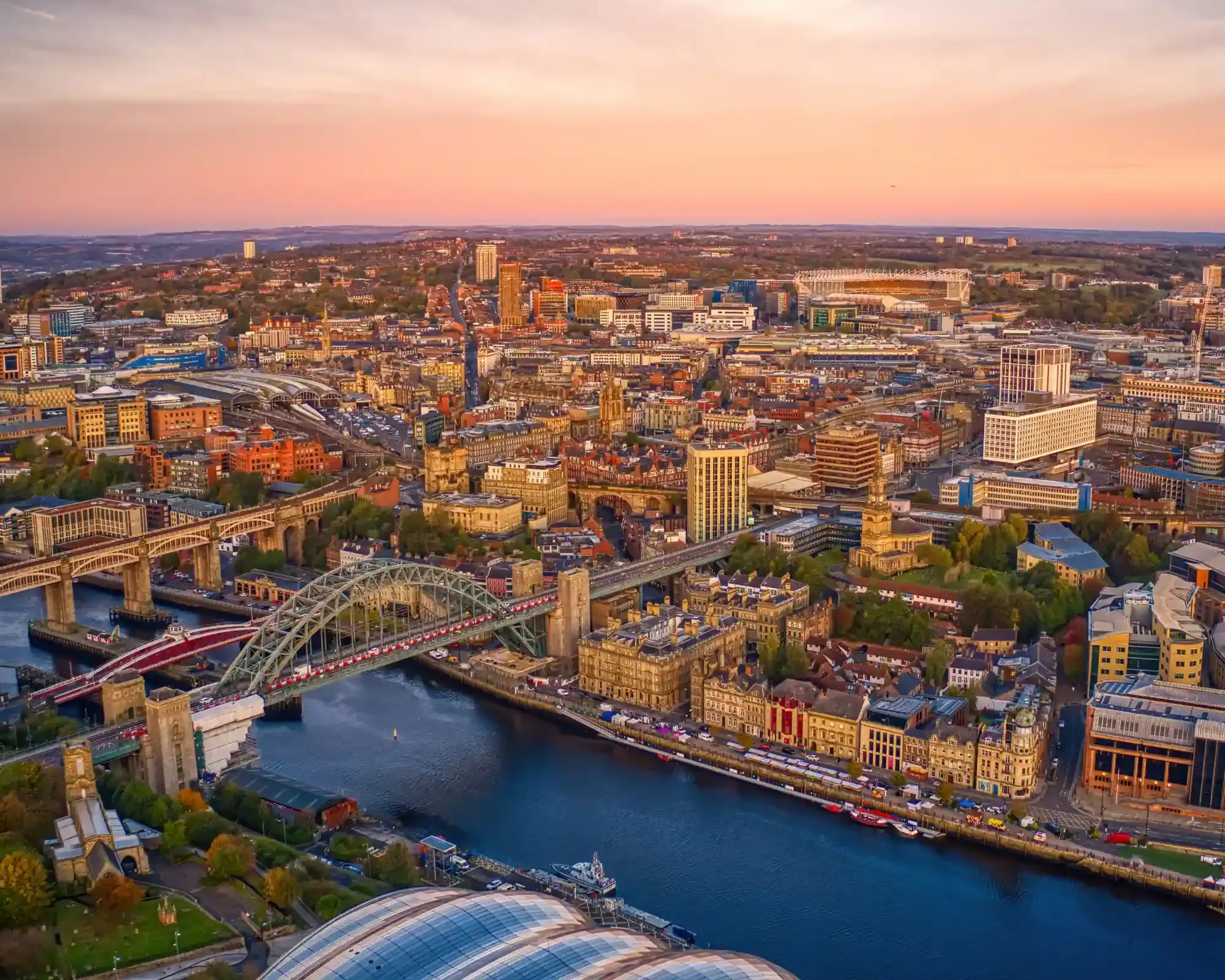 Aerial view of Newcastle at sunset, with the Tyne Bridge, the Quayside and the city centre beyond.