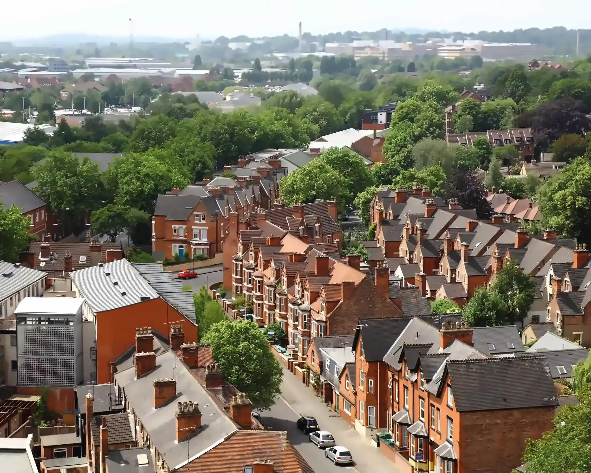 Aerial view of rows of red-brick Victorian terraced houses in Nottingham, set among leafy green trees, with the city stretching into the distance.