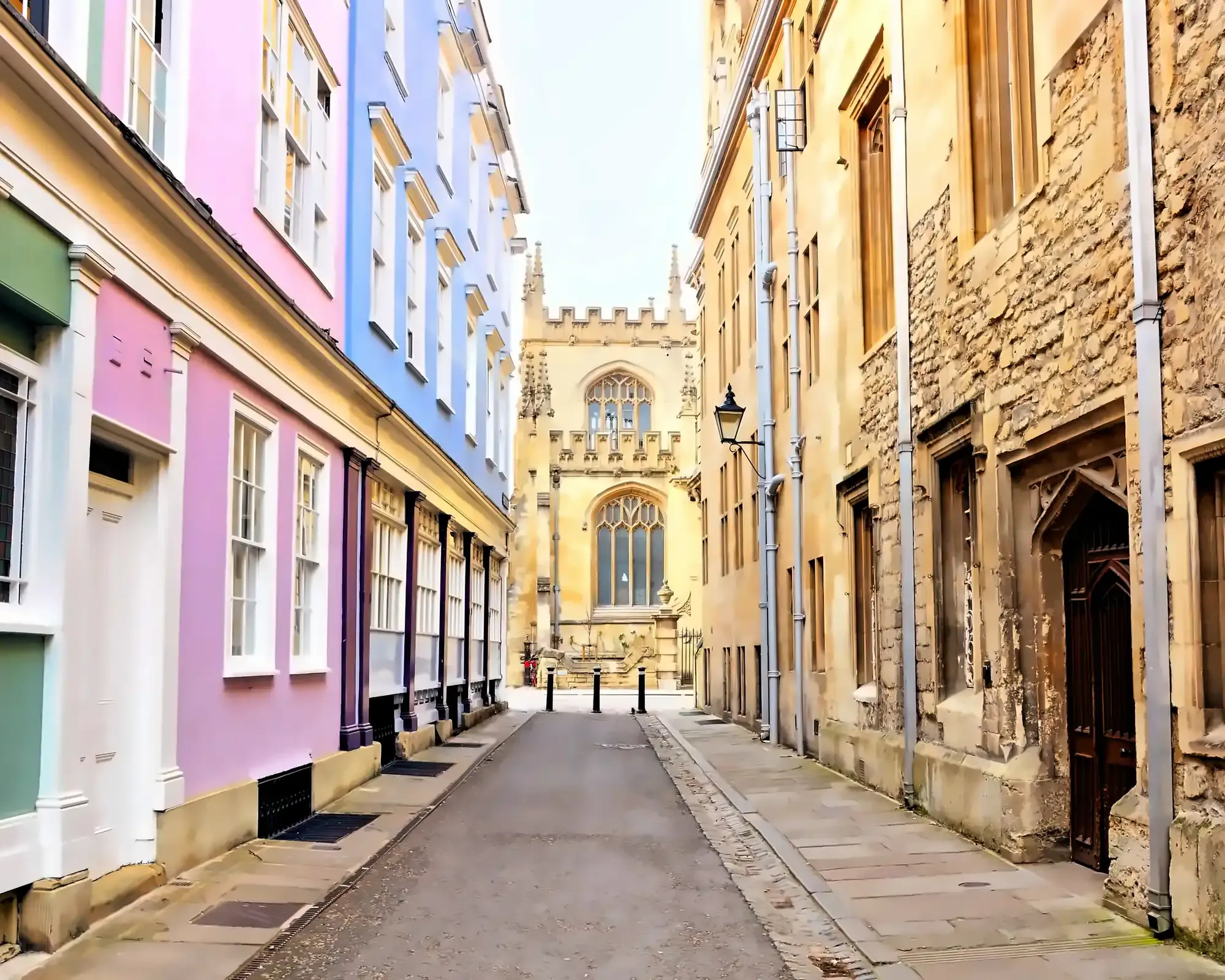 A narrow lane in Oxford with pastel-painted houses on one side and old stone college buildings on the other, leading to a Gothic chapel.