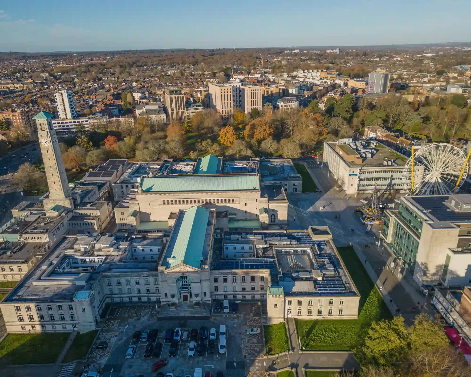 Aerial view of Southampton Civic Centre and its clock tower on a sunny autumn day, with a big wheel nearby and trees and city streets stretching beyond.