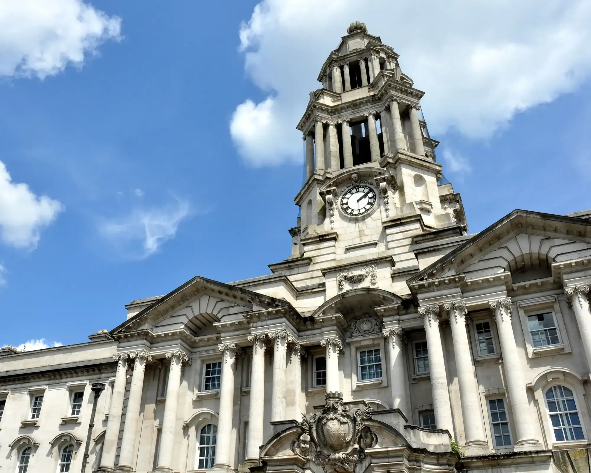 Stockport Town Hall’s white stone facade and clock tower against a blue sky.