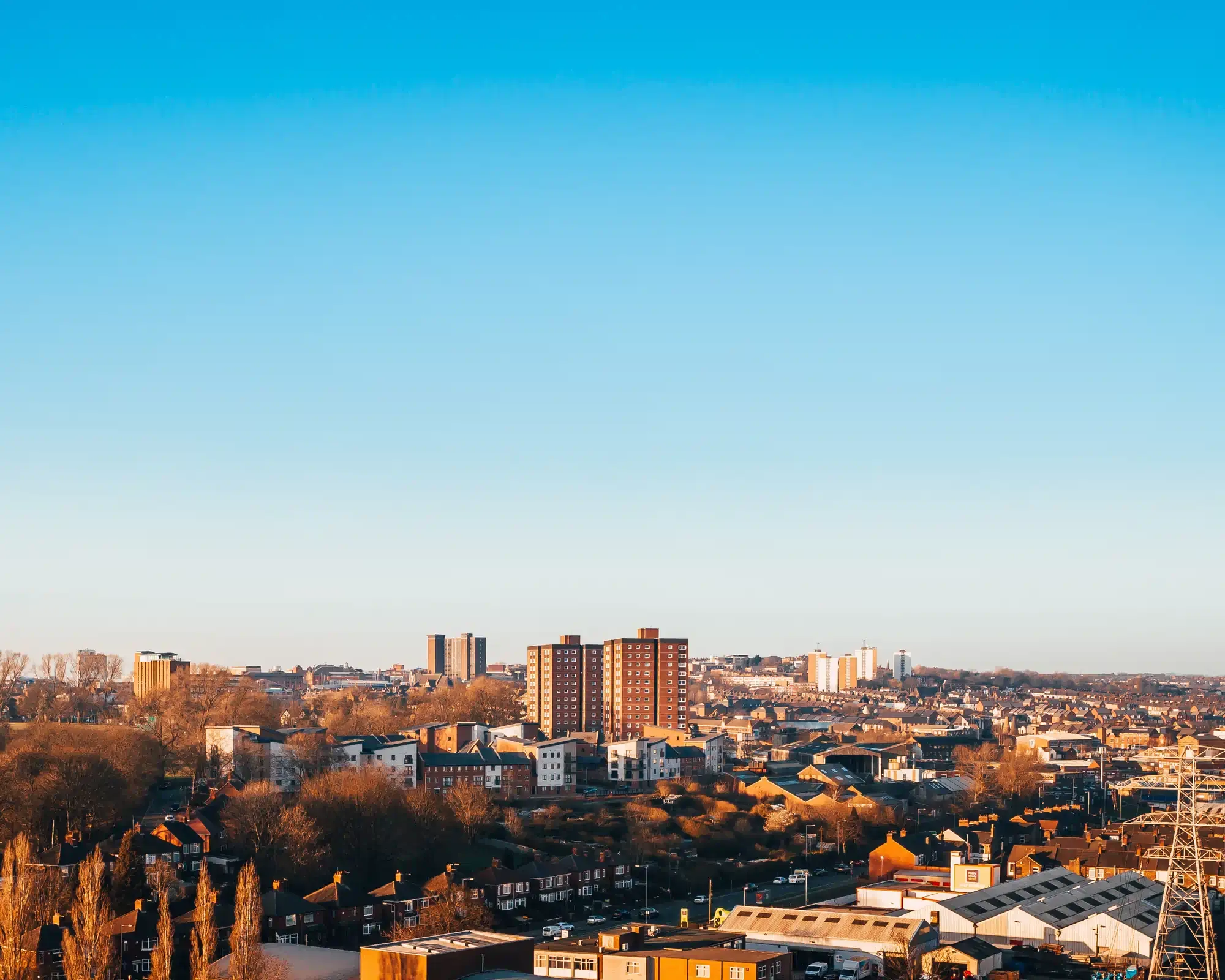 Stoke-on-Trent at golden hour, with red-brick tower blocks rising above rows of houses and bare trees under a clear blue sky.