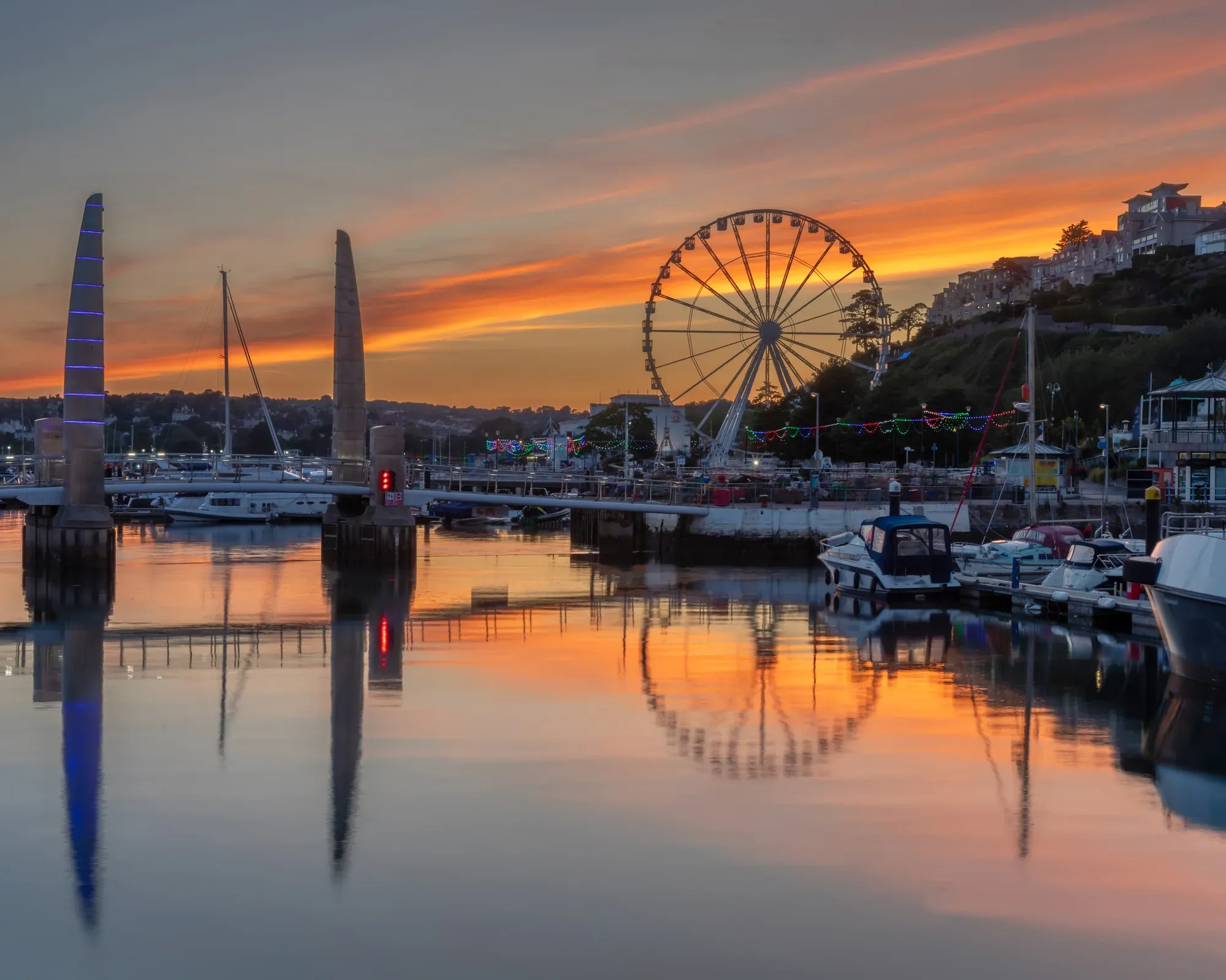 Torquay harbour at sunset, with the footbridge towers and the big wheel reflected in the water.
