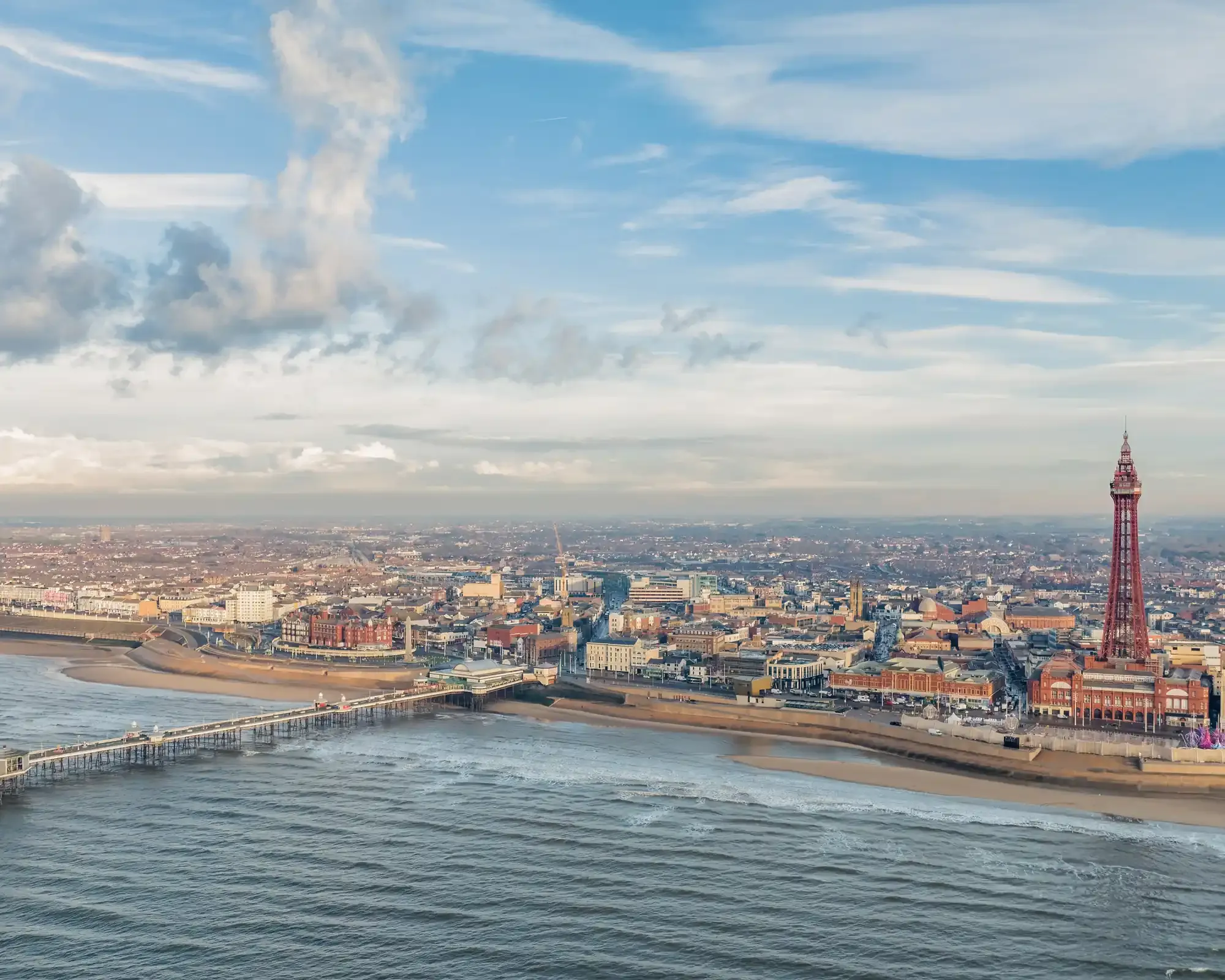 Aerial view of Blackpool seafront with North Pier stretching into the Irish Sea and Blackpool Tower rising above the town centre.